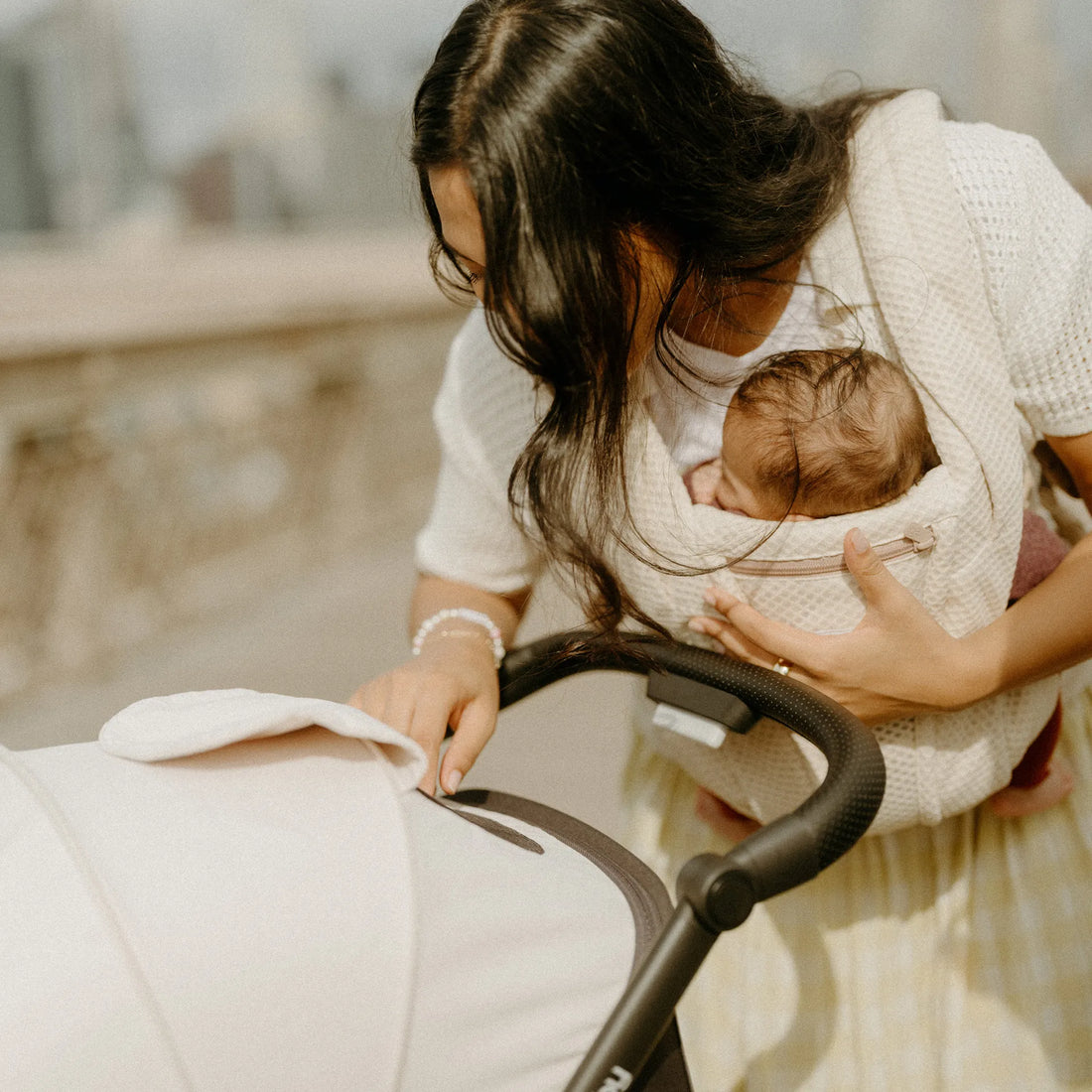 Femme tenant un bébé dans un porte-bébé beige regardant une poussette