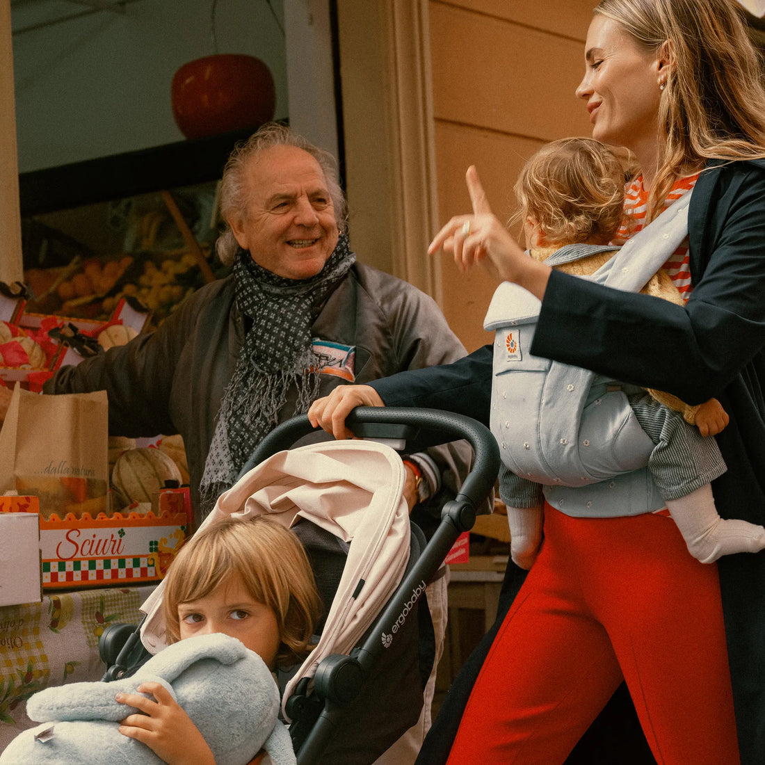 Eine Frau, die ein Baby in einer Babytrage hält, Babytrage ein Kleinkind im Kinderwagen und unterhält sich dabei mit einem Mann