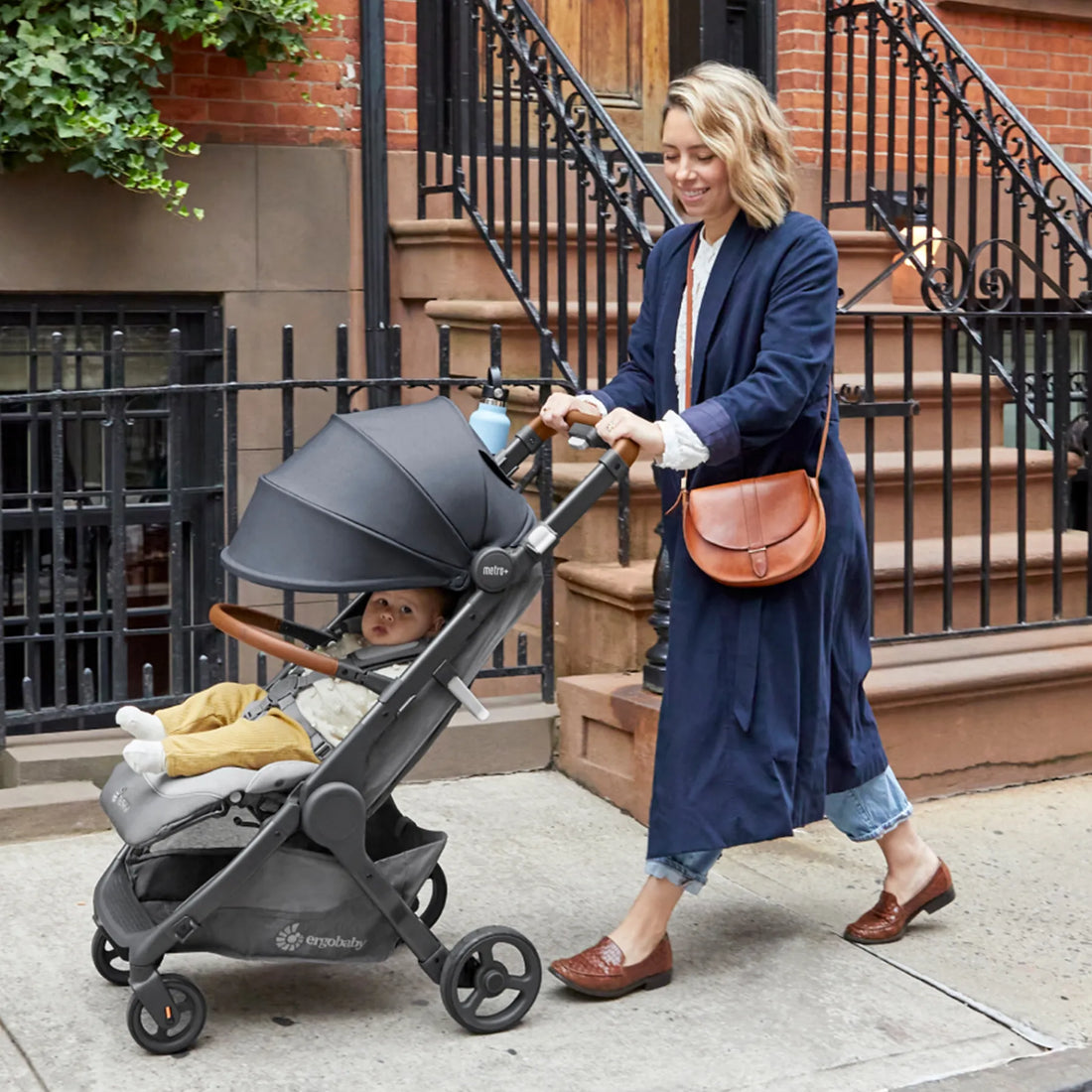 Eine Frau in einem Mantel schiebt einen Kinderwagen die Straße entlang 