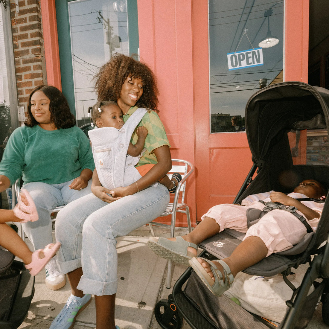 Eine Frau, die ein Baby in einer Babytrage hält, Babytrage sie auf ein Baby herabblickt, das in einem Kinderwagen schläft