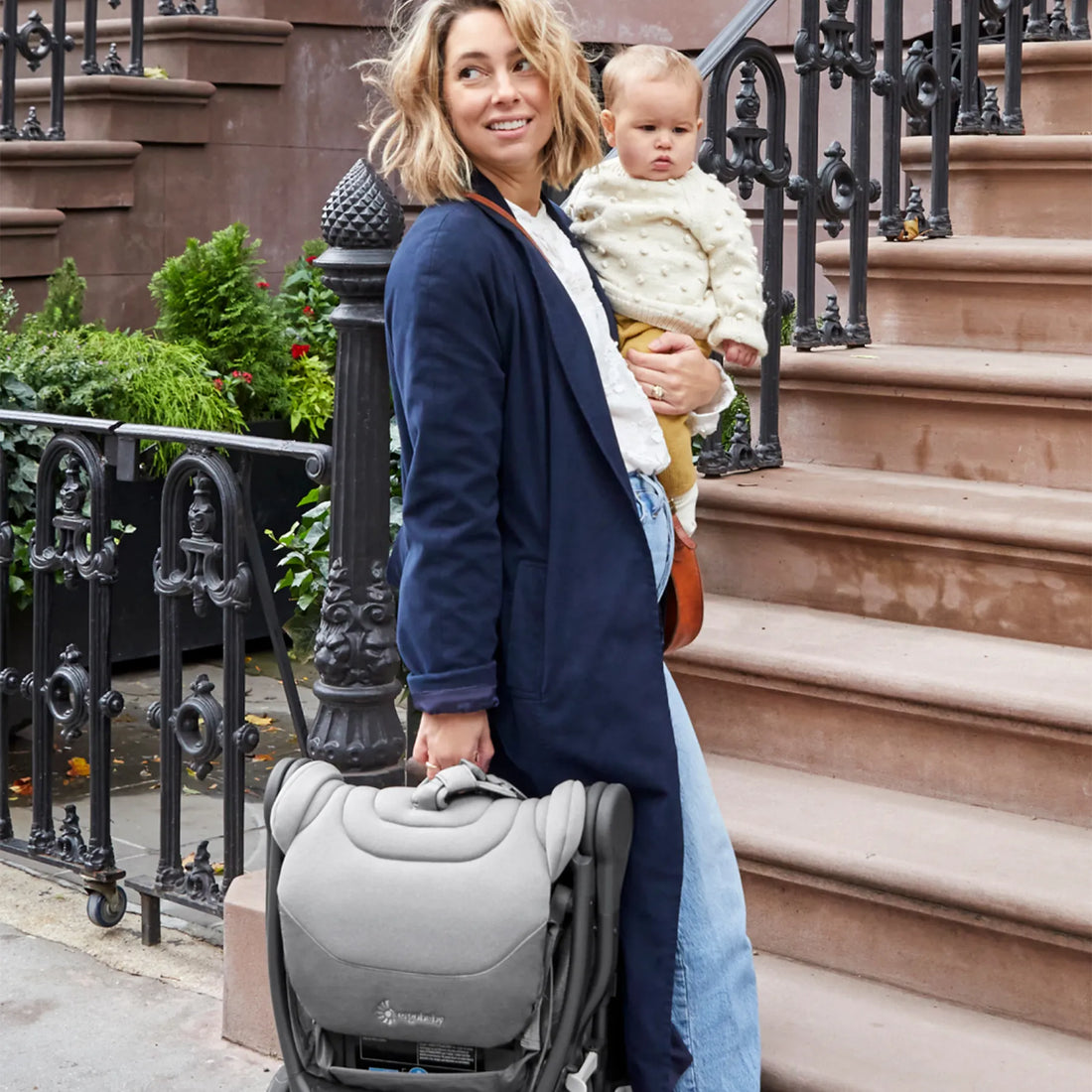 Frau, die ein Baby auf der Hüfte hält und einen Reisekinderwagen dabei hat 