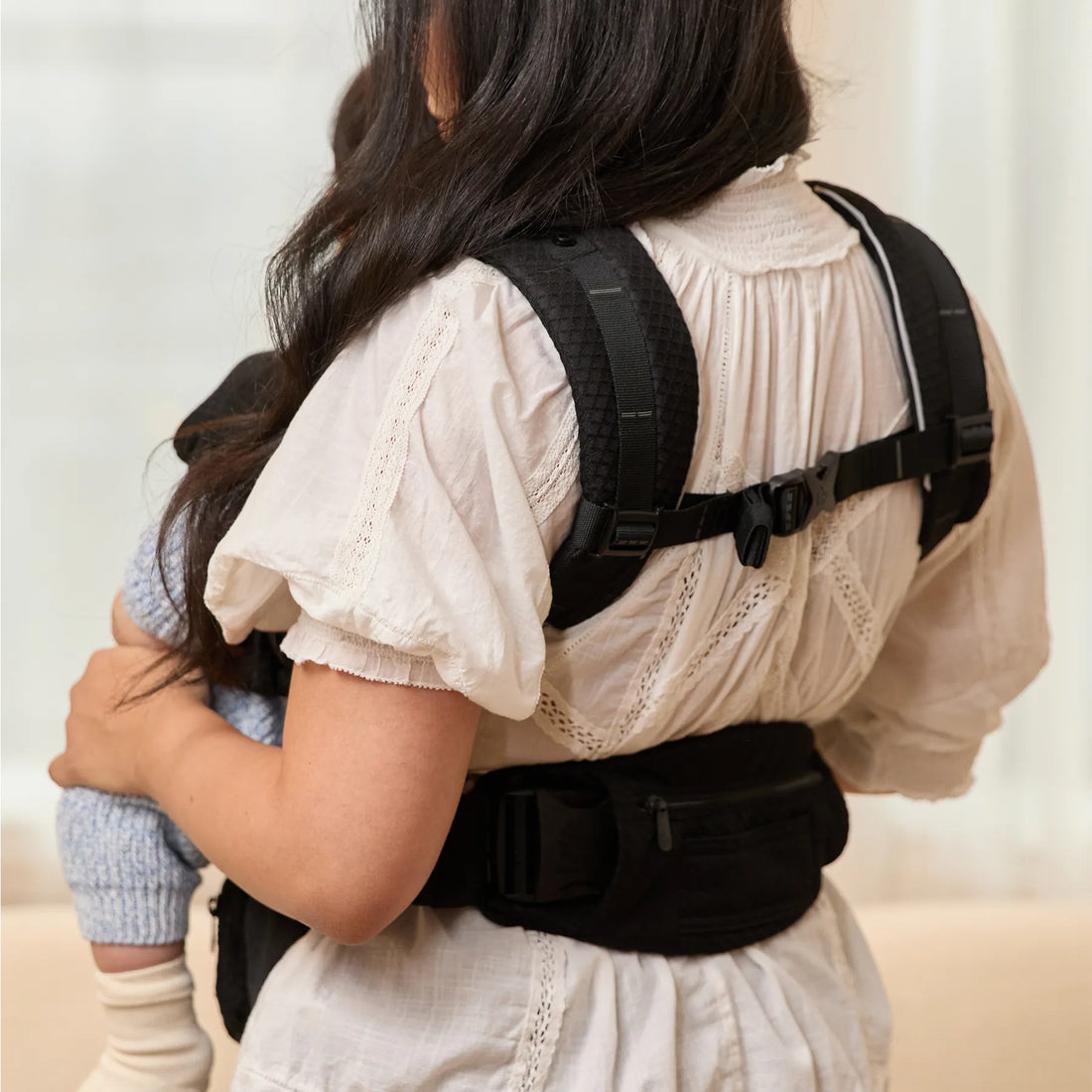 Rückenansicht einer Person, die einen schwarzen Babytrage trägt und ein Baby Babytrage 