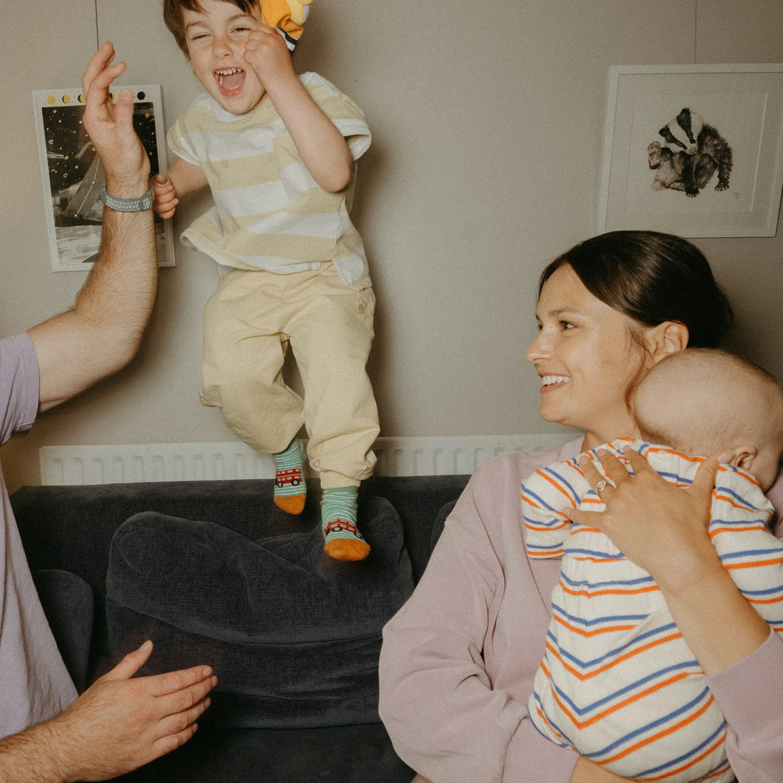 Eine Frau hält ein Baby im Arm, während zwei Kleinkinder neben ihr spielen