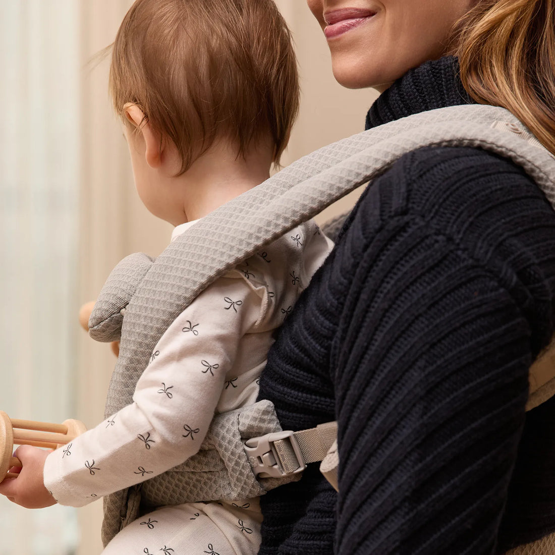 Femme tenant un bébé dans un porte-bébé gris avec le bébé tourné vers l’extérieur