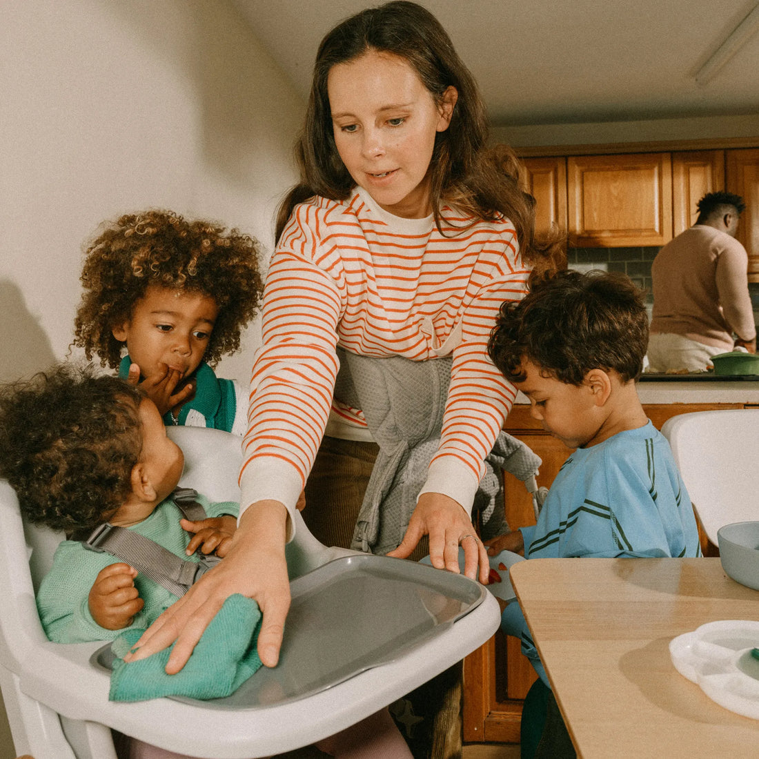 Eine Frau, die einen Hochstuhl reinigt, während zwei Kleinkinder neben ihr stehen