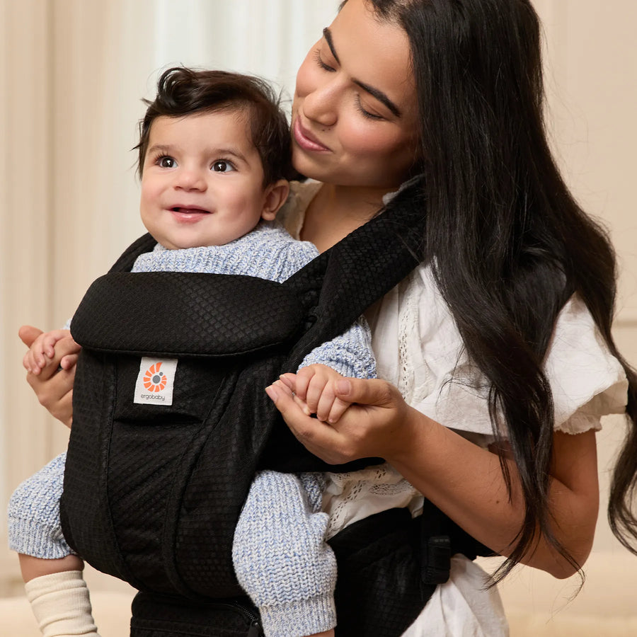 Woman holding a baby facing out in a black baby carrier