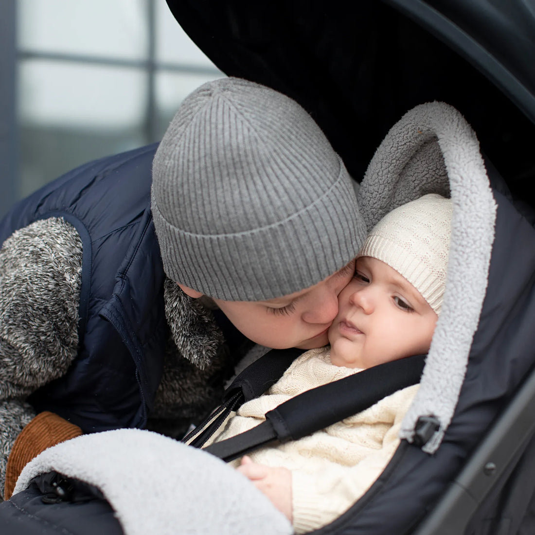 Ein Kind beugt sich vor, um ein Baby im Kinderwagen zu küssen 