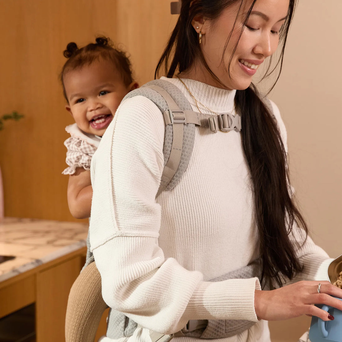 Frau, die einen grauen Babytrage trägt Babytrage ihr Baby auf dem Rücken Babytrage
