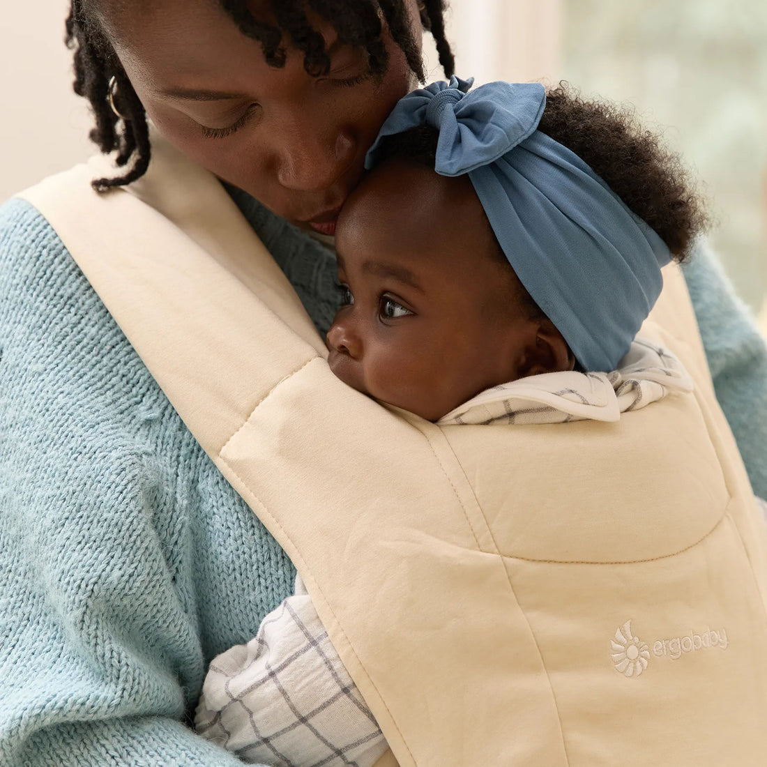 Frau, die ein Baby in einer beigen Babytrage hält