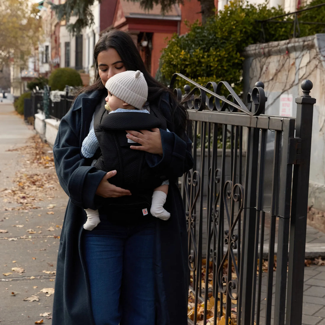 Frau in einem Mantel, die ein Baby in einem schwarzen Babytrage hält