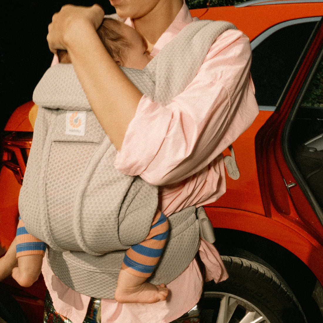 Frau, die ein Baby in einem grauen Babytrage einem Auto hält