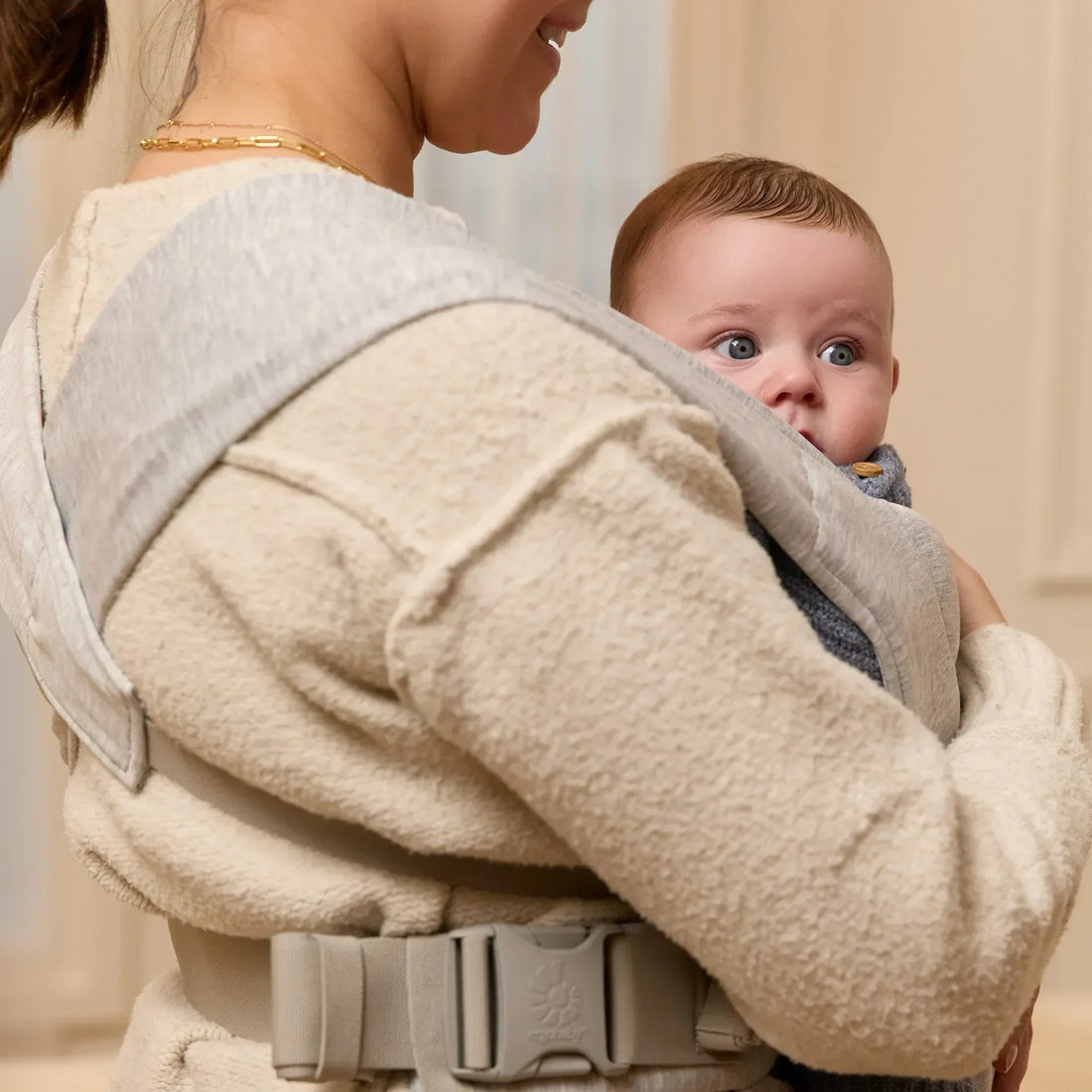 Frau, die ein Baby in einer grauen Babytrage hält