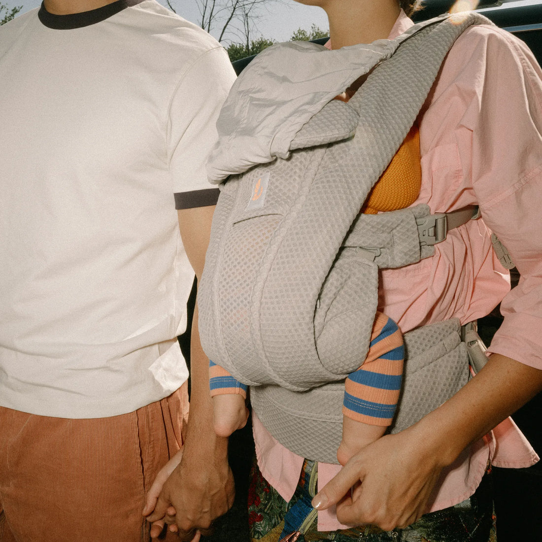 Frau, die ein Baby in einem Babytrage trägt Babytrage die Hand eines Mannes hält