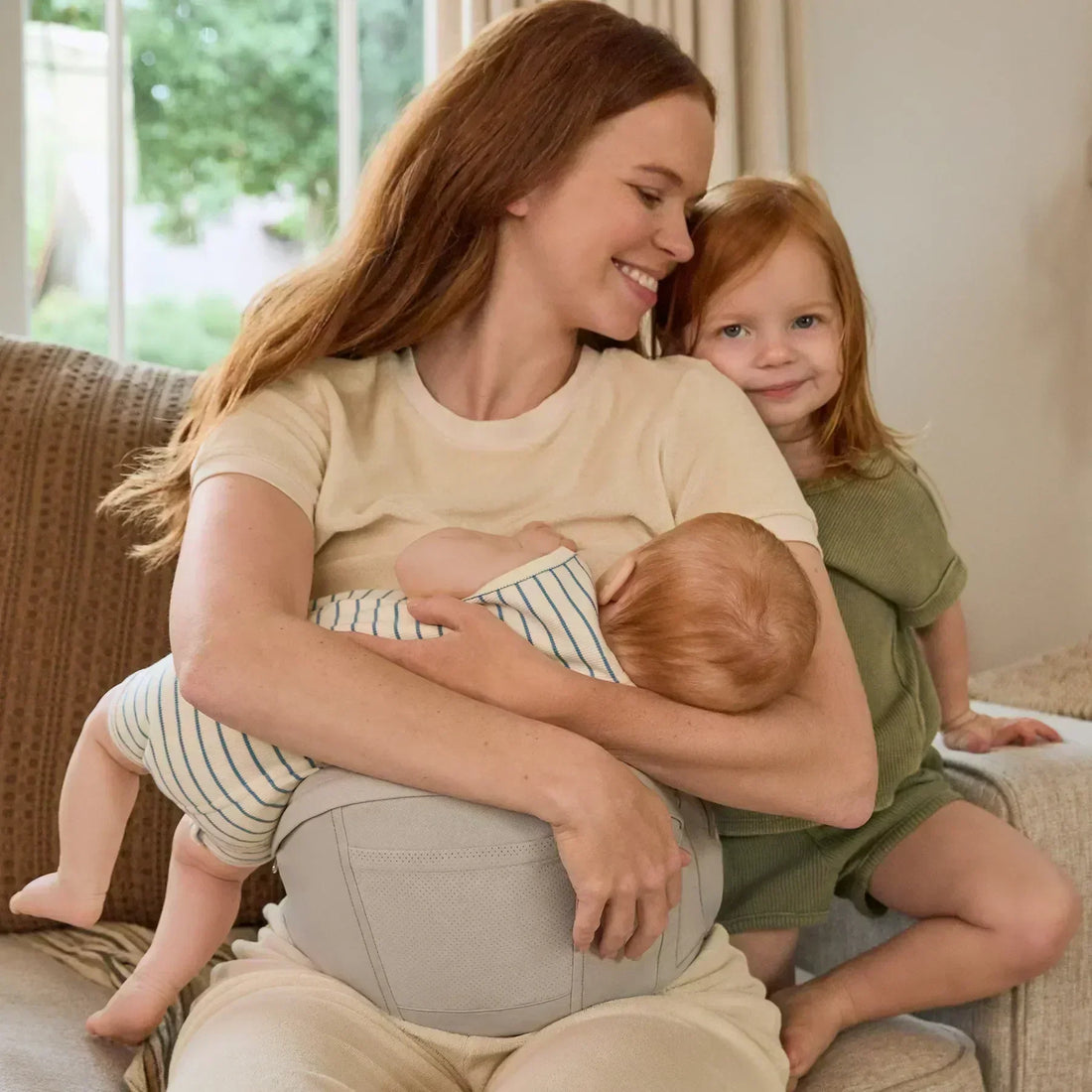Eine Frau, die ein Baby stillt, während sie auf einem Sofa sitzt und ein weiteres Kind neben sich hat