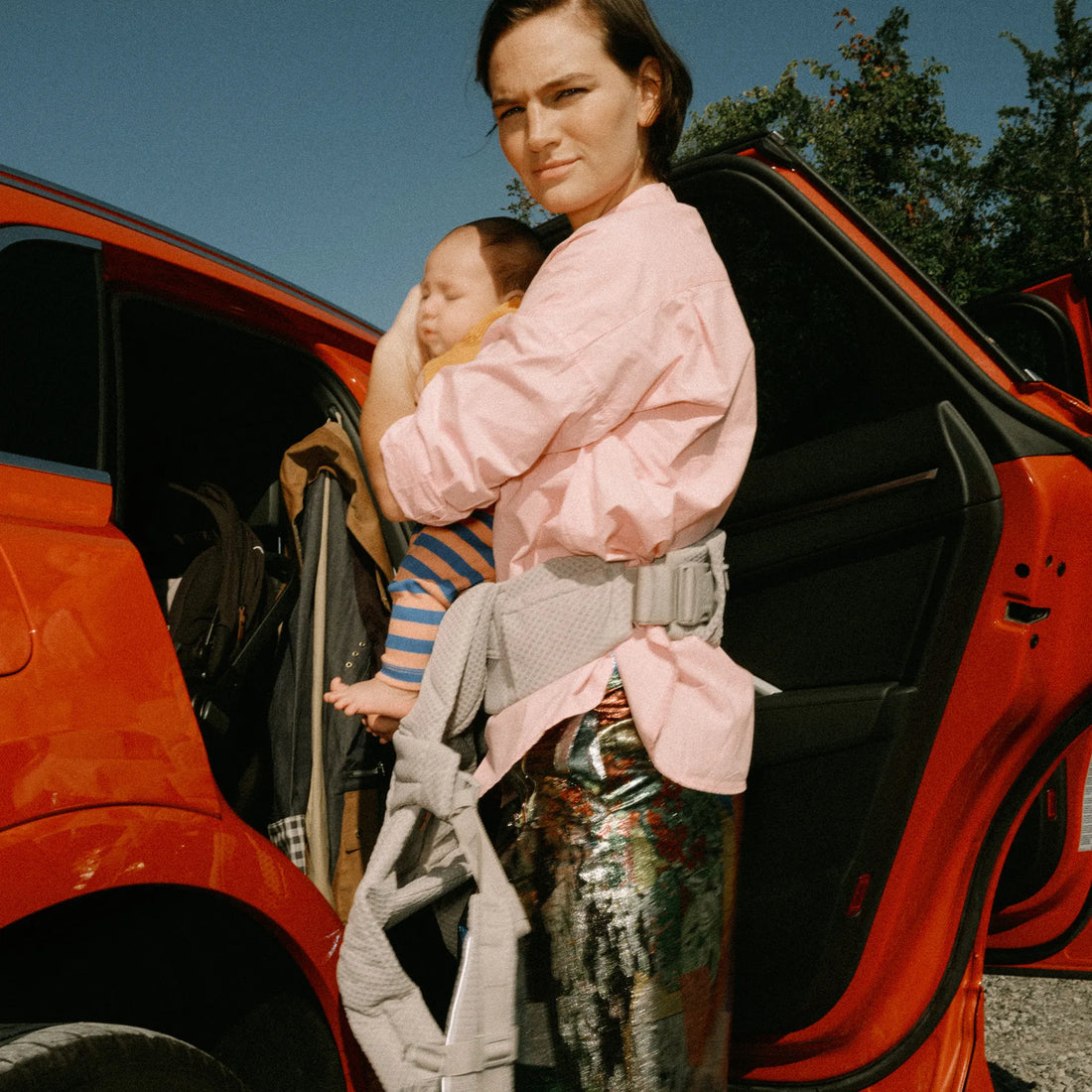 Frau, die ein Baby in einem Babytrage einem Auto hält