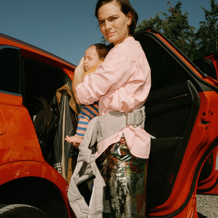 Una donna con un bambino nel marsupio accanto a un'auto