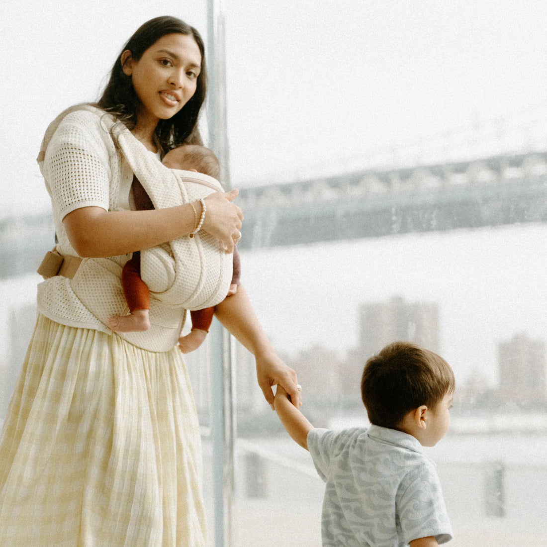 Eine Frau, die ein Baby in einem weißen Babytrage trägt Babytrage die Hand eines Kleinkindes hält