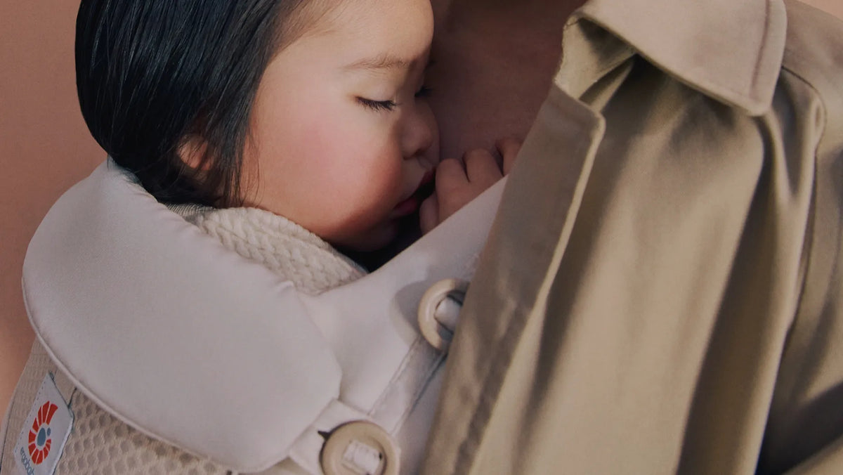 Ein Kind in einer omni classic Babytrage einem Soft-Focus-Hintergrund