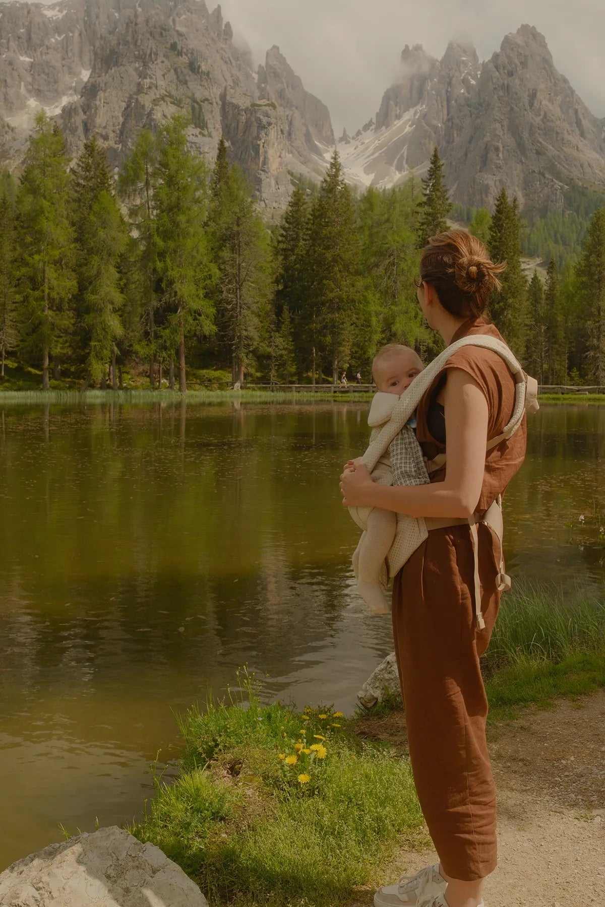 Eine Frau, die ihr Baby inBabytrage  omni deluxe Babytrage hält,Babytrage einem See mit Bergen im Hintergrund